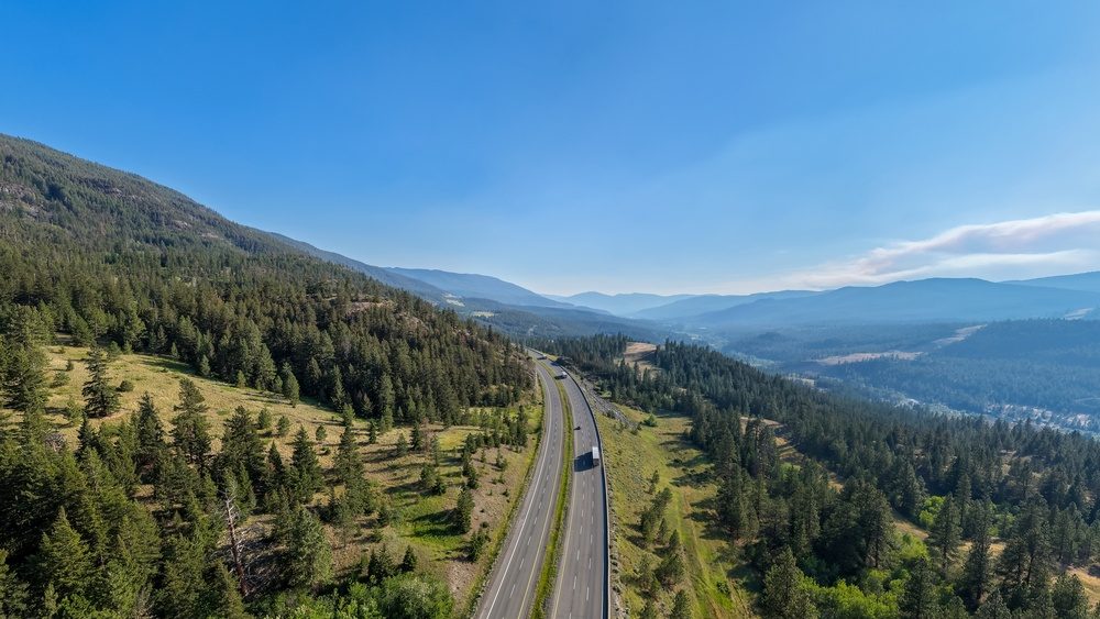 Aerial view of the Trans-Canada Highway near Merritt, British Columbia, Canada winding through forested mountains and clear blue sky.