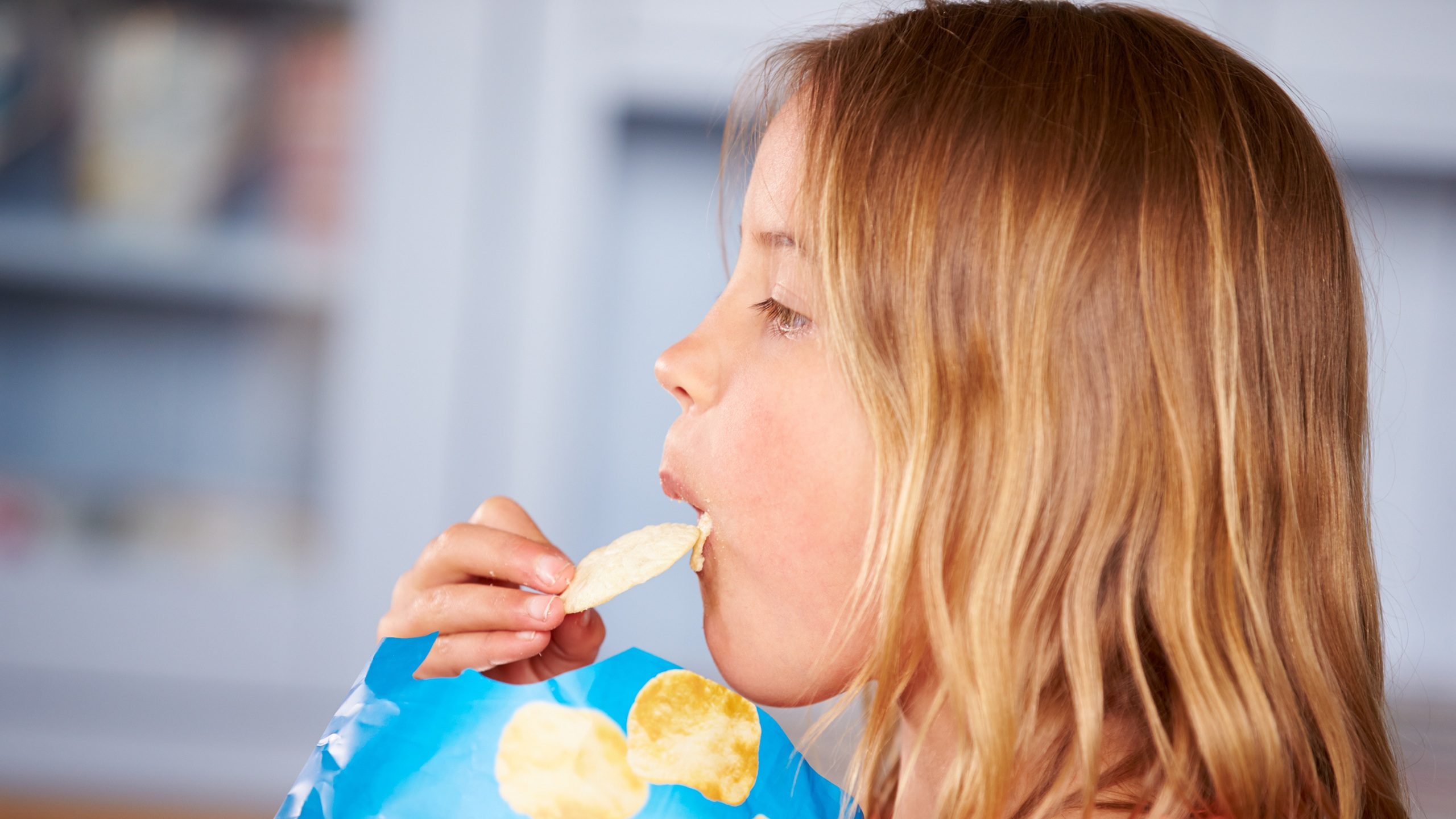 Young Girl Sitting At Table Eating Potato Chips