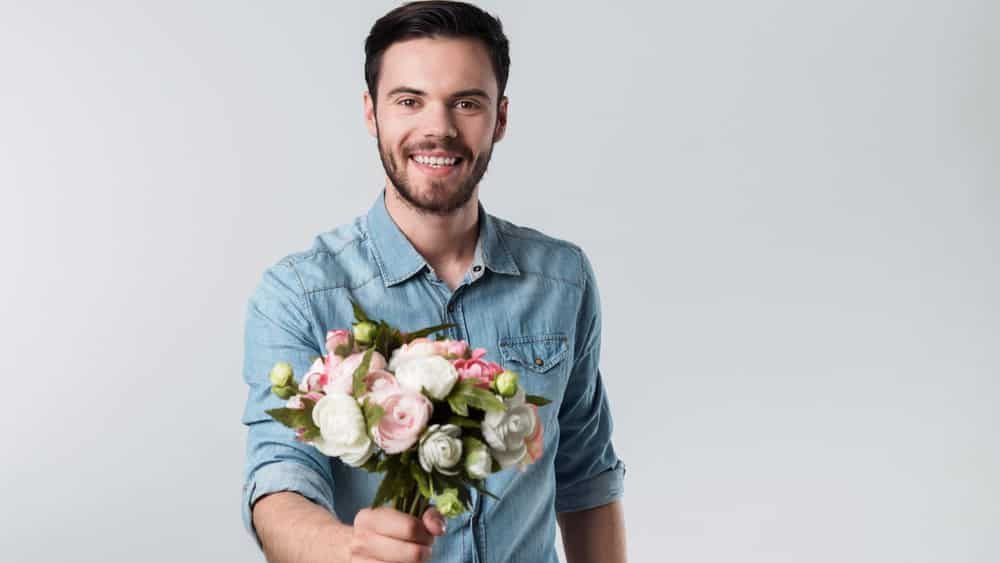 Happy handsome young man holding a bunch of flowers.