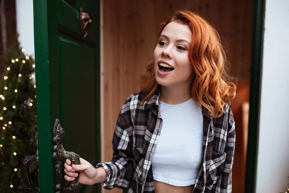 Image of pretty young woman with red hair open the door. Looking aside.