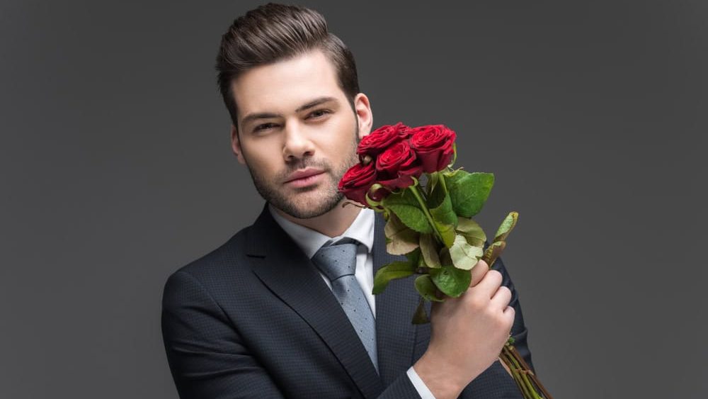handsome man in suit holding bouquet of red roses, isolated on grey