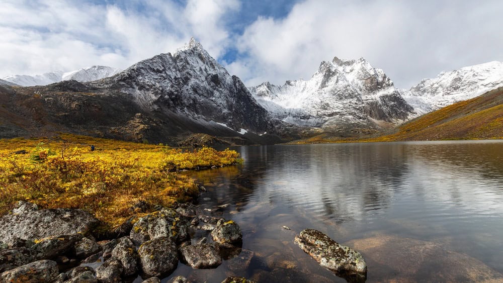 Beautiful View of Scenic Alpine Lake, Rocks and Snowy Mountain Peaks in Canadian Nature. Season change from Fall to Winter. Taken at Grizzly Lake in Tombstone Territorial Park, Yukon, Canada.