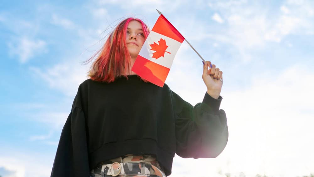 Student girl teenager with Canada flag in hand, blue sky with clouds background. Canada, education and youth, patriotism people concept