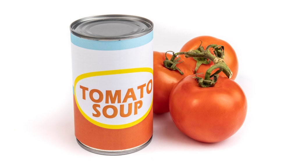 A generic labeled can of tomato soup with a bunch or ripe red tomatoes on the vine isolated on white