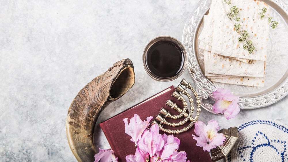 Metal plate with matzah Kiddush Cup, Shofar horn on a light background presented as a Passover seder feast or meal with copy space. Jewish traditional objects, yarmulke, Tallit, Prayer book