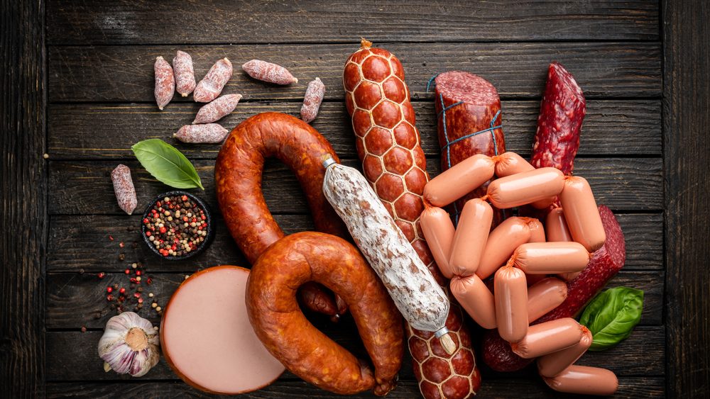 Set of different types of sausages, salami and smoked meat with basil and spices on wooden background. Top view.