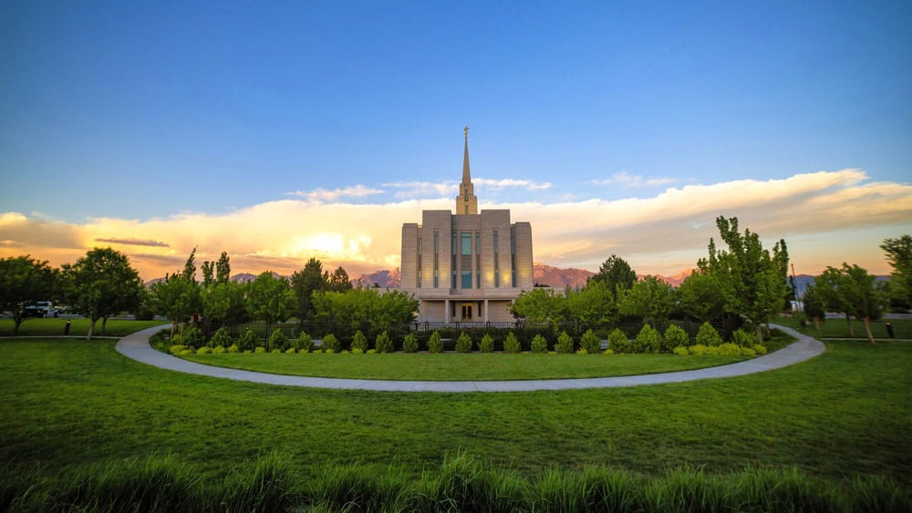 A front view of a mormon church in Utah at the sunset in a beautiful park with green grass and trees