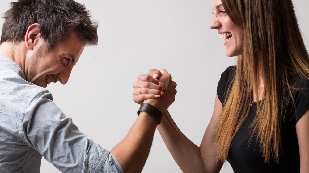 Man and woman, playfully defiant, engage in arm wrestling, embodying the dichotomy of friends and lovers, rivals and competitors, but always with a sense of fairness and fun