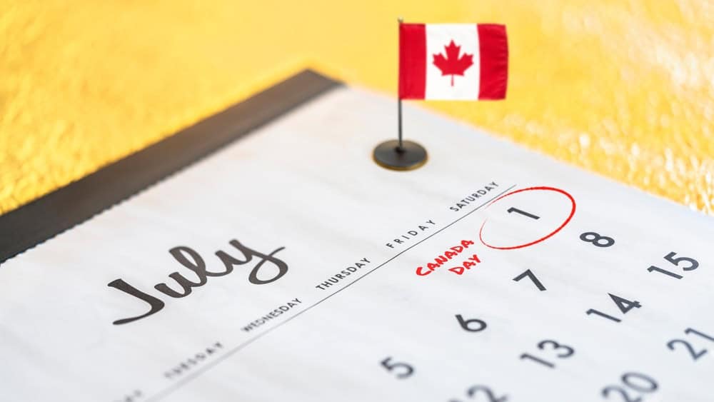 Close-up photograph of a calendar dedicated to the month of July and particularly the date of July 1 surrounded in red marker to celebrate Canada's National Day with a mini desk flag on the background