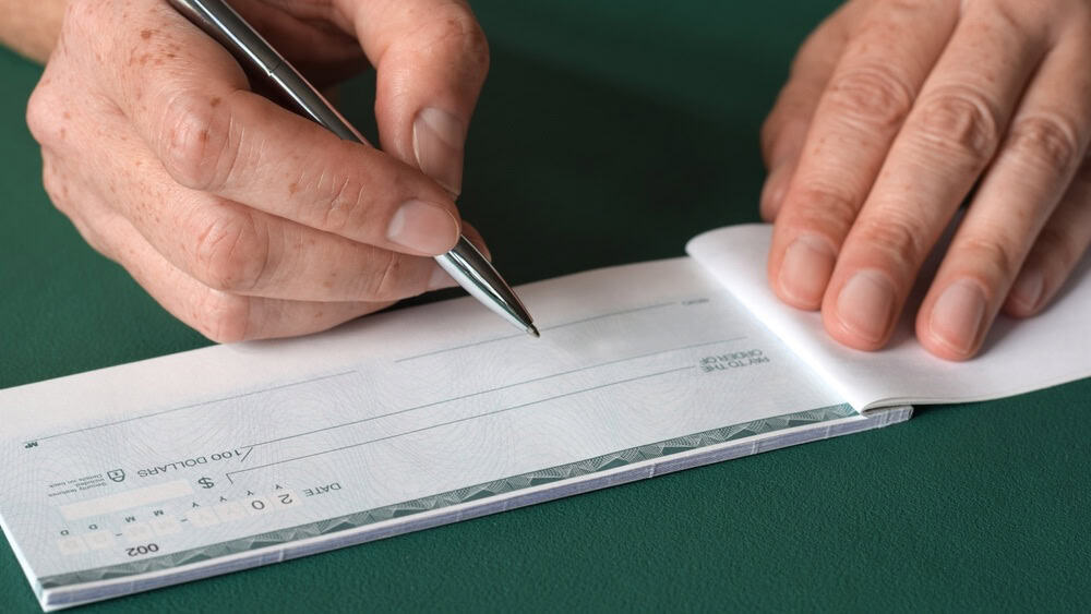 Closeup woman's hands writing bank cheque on green background
