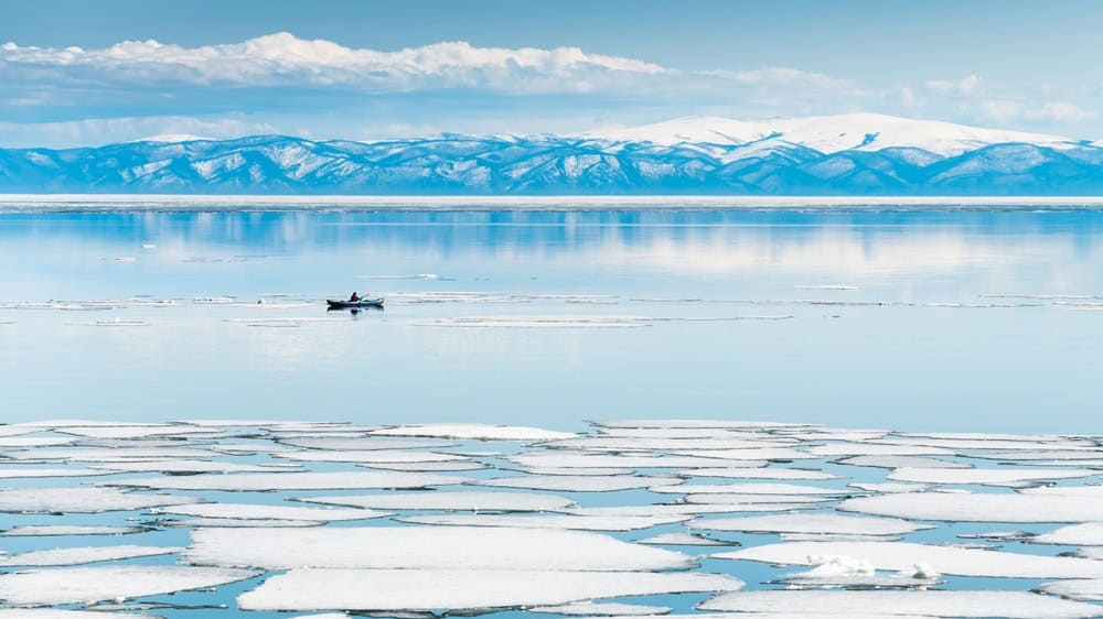 Melting ice on Baikal lake. Kayak sailing between ice floes on the lake. Baikal, Siberia, Russia. Beautiful spring landscape.