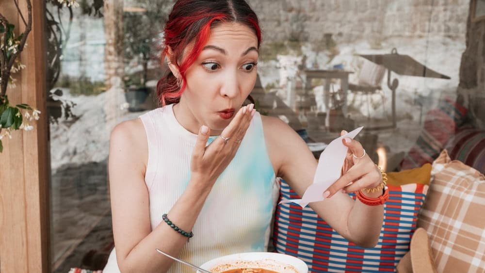 Shocked woman at a restaurant confronted with an unexpectedly expensive bill.
