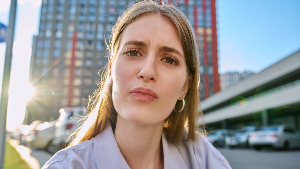 Close-up selfie portrait of teenage confused female looking at web camera