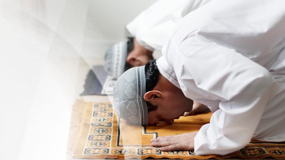 Two men in traditional Islamic attire, engaged in prayer. Islamic men, dressed in white, are bowing in prayer. Islamic prayer scene highlights the men's religious devotion and traditional attire.