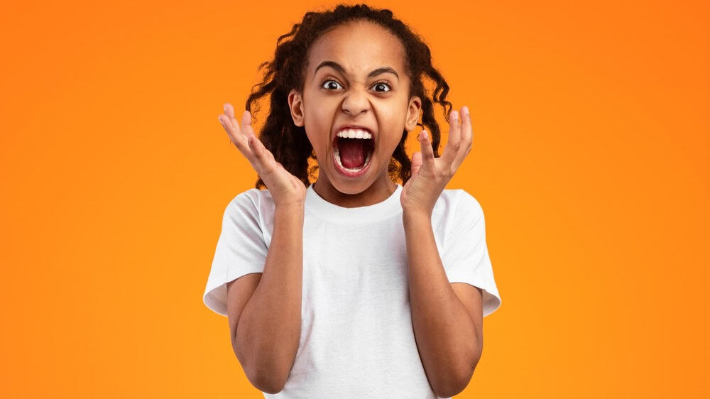 Anger Concept. Portrait of mad African American girl shouting and gesturing. Furious teen screaming loud, tired of school and problems, expressing negative emotions, isolated on yellow studio wall