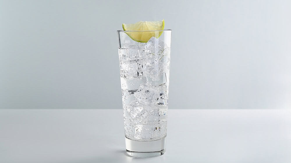 Refreshing soda water with ice cubes and slice of lime in glass on white table against light background