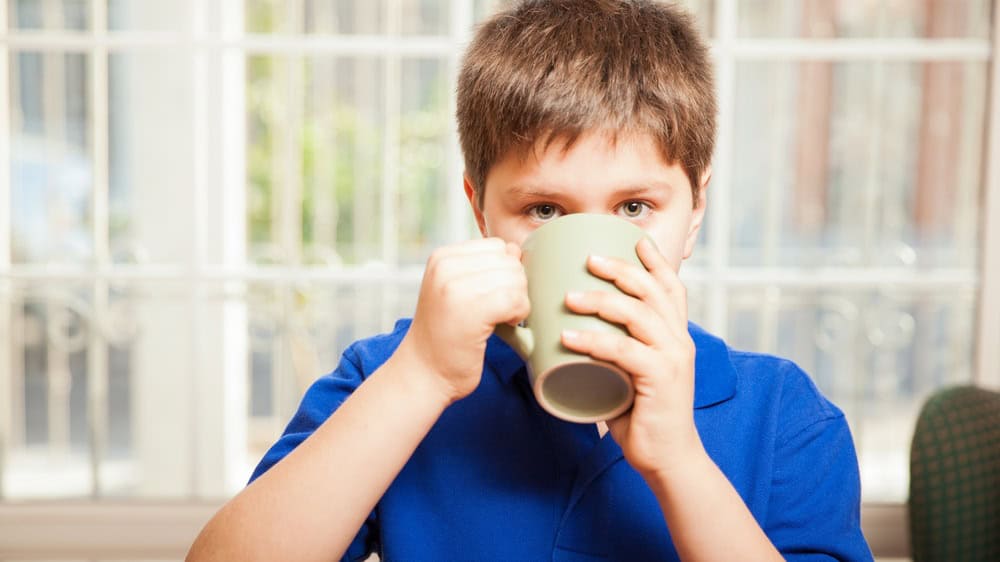 Young boy drinking some coffee from a mug and making eye contact