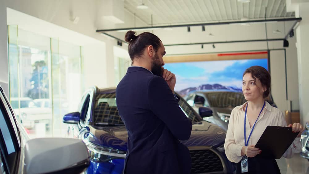 Saleswoman in dealership talking with client, trying to grasp their preferences for vehicle type, brand and price range to gain insights into what might sway their purchasing decision, camera B