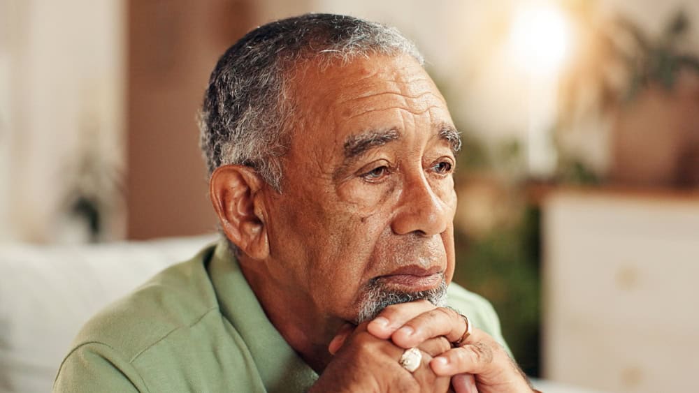 Sad, senior man or thinking in home with retirement loneliness, grief or remember memory with nostalgia. Face, mental health or elderly person with depression on sofa for loss, reflection or dementia