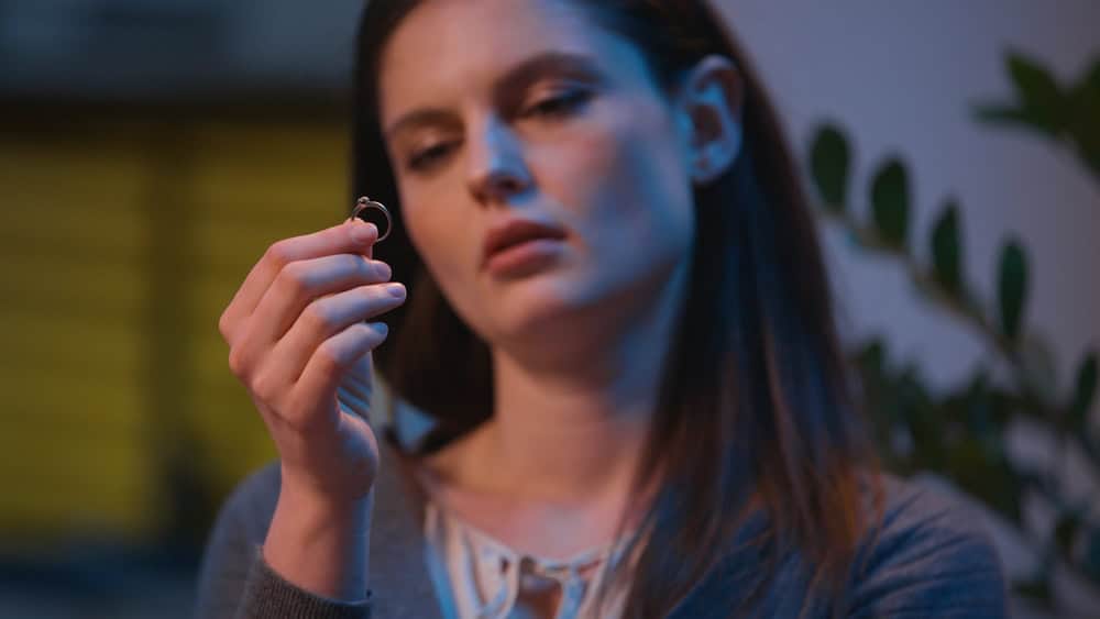 Caucasian woman sad at home night evening upset take off wedding ring frustrated girl female wife regret thinking marriage problem breakup divorce betrayal engagement heartbreak difficult decision
