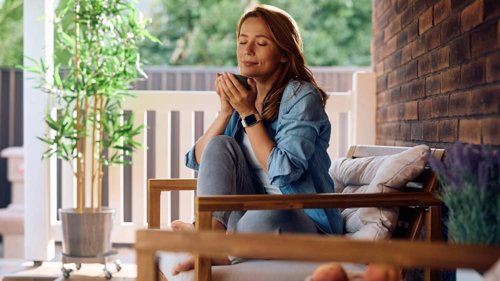Smiling woman with eyes closed enjoying in cup of coffee while relaxing on the porch. Copy space. 