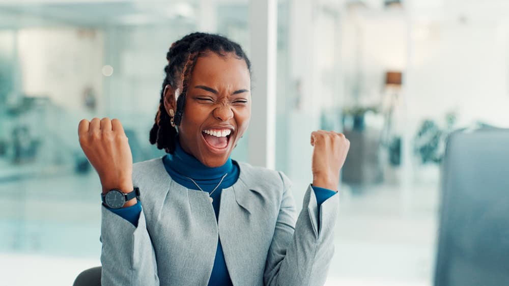 Business, woman and celebration with computer in office for article success, trending story and reward. Journalist, black person and tech with victory fist for blog recognition and career achievement