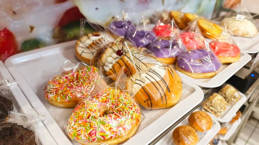 Colorful Assortment of Donuts and Pastries Displayed on Shelves, Freshly Baked Donuts and Sweet Treats in Protective Packaging on Display