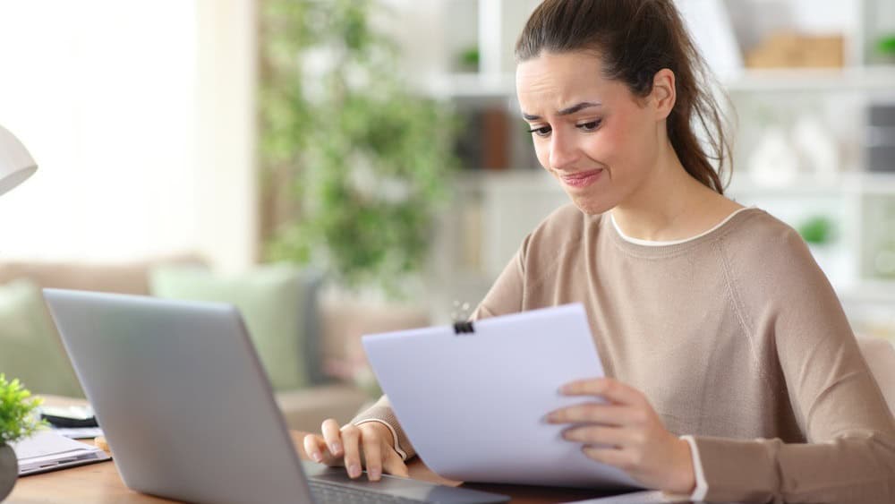 Worried freelance worker reading paper documents working online at home