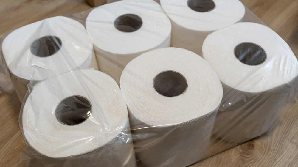 A pack of six rolls of paper towels enclosed in transparent plastic, placed on a wooden floor. Ideal for cleaning or household tasks, showcasing a practical kitchen item.