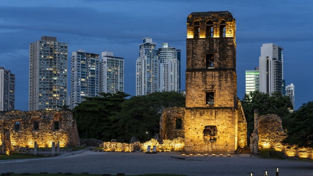 Old Panama la Vieja ruins, including the iconic tower, stand illuminated at dusk, creating a stark contrast against the towering modern skyscrapers of Panama city - stock photo