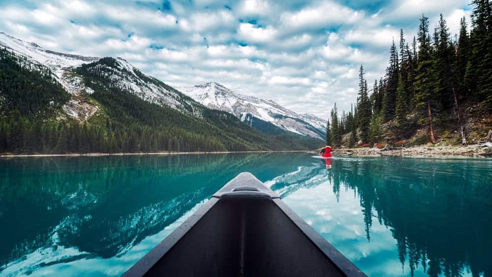 POV Shot scenic view of canoe rowing in turquoise Maligne Lake with Rocky Mountains and pine forest reflection in Jasper national park, Alberta, Canada