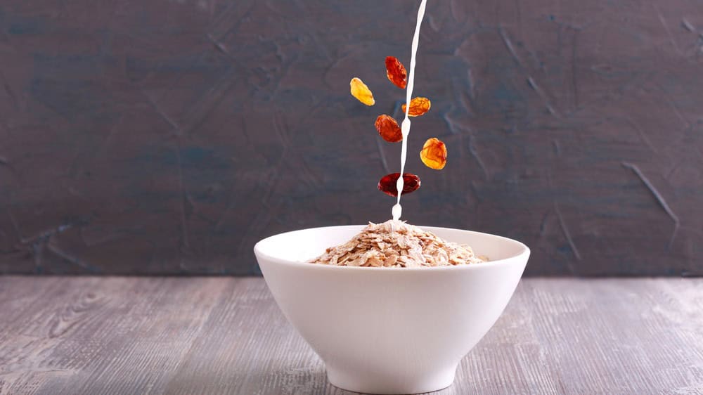 Oat flakes in a bowl, raisin and milk above