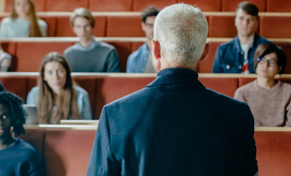 Camera Facing Class: College Professor Gives a Lecture to a Classroom Full of Multi Ethnic Students. Talented Speaker Captures Audience Attention.