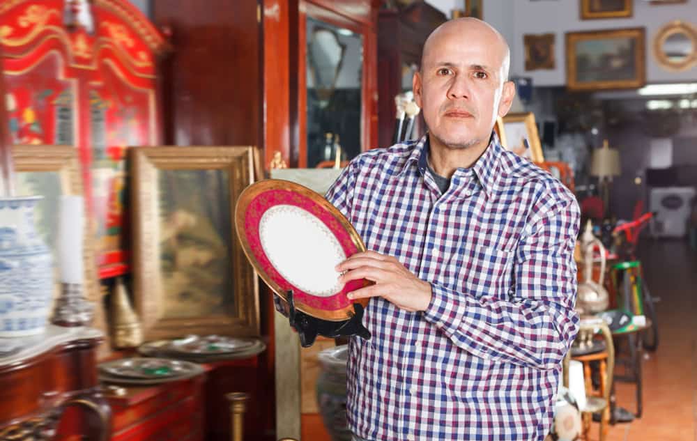 Serious man carefully examining antiques in store