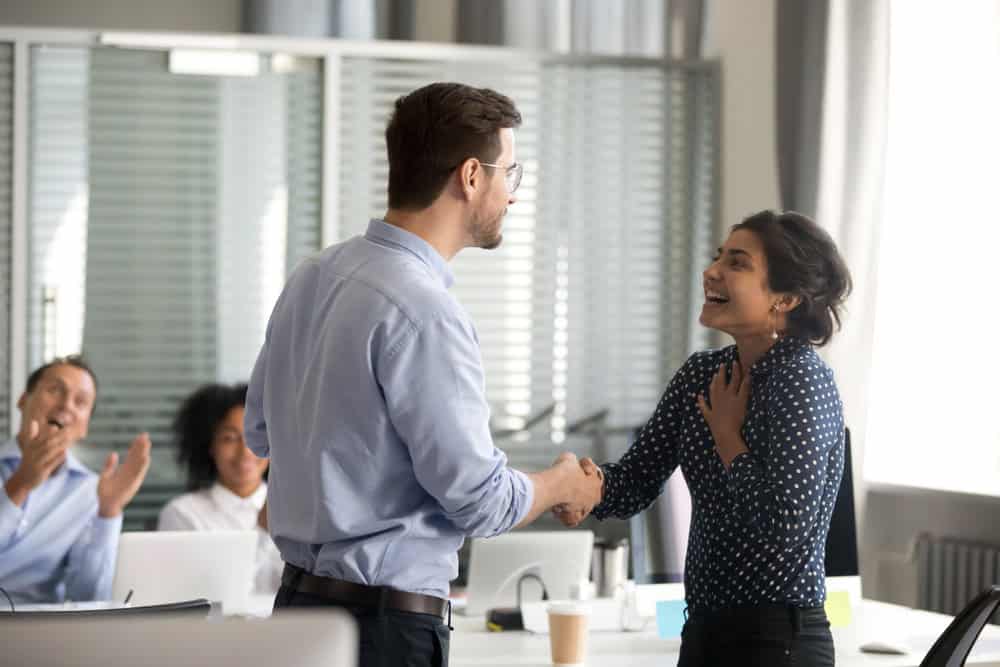 Team leader motivating handshaking female Indian excited employee, congratulate with promotion, business achievement, thank for good result, work, expressing respect, support, colleagues applaud