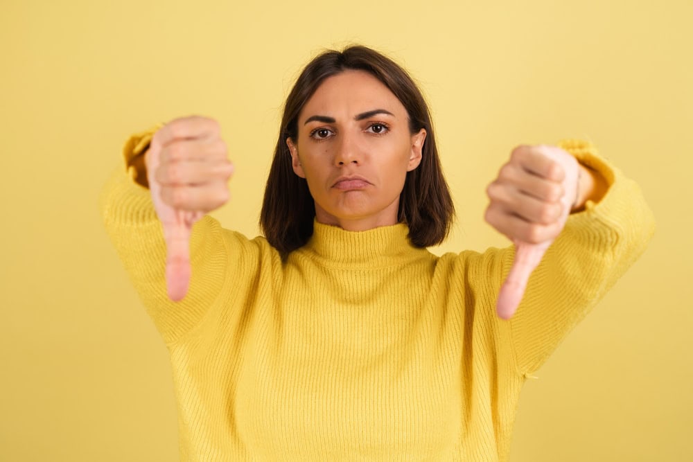 Young woman in yellow warm sweater unhappy disappointed shows thumb down
