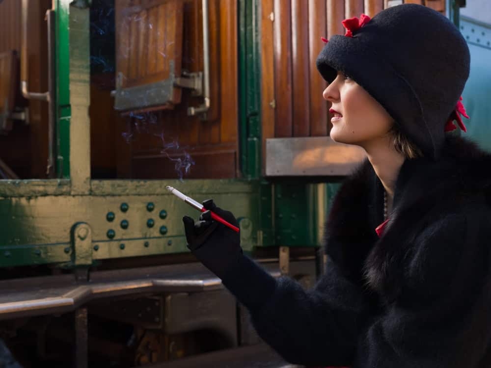 Attractive young woman in red 1920s flapper dress and cloche hat travelling by antique steam train