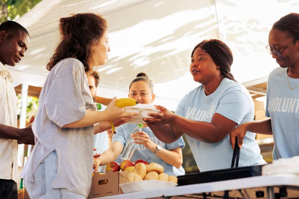 Multiracial volunteers handing out meal donations to the needy at a food drive. Image showing voluntary people generously supporting the homeless and those experiencing poverty and hunger.