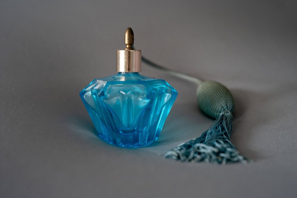 A vintage blue crystal perfume bottle with a bulb atomizer sits elegantly on a dark surface, reflecting soft light beautifully.