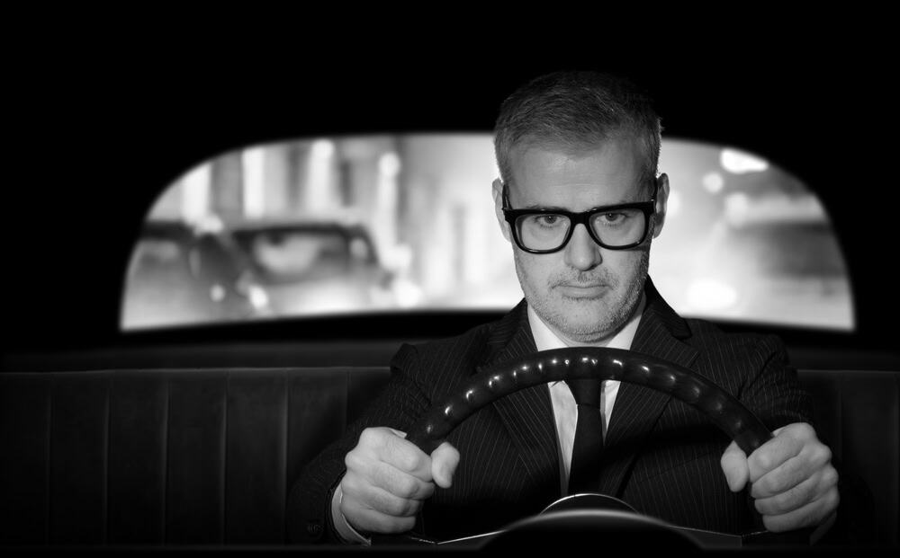 Vintage style businessman holding the steering wheel and driving his car, film noir
