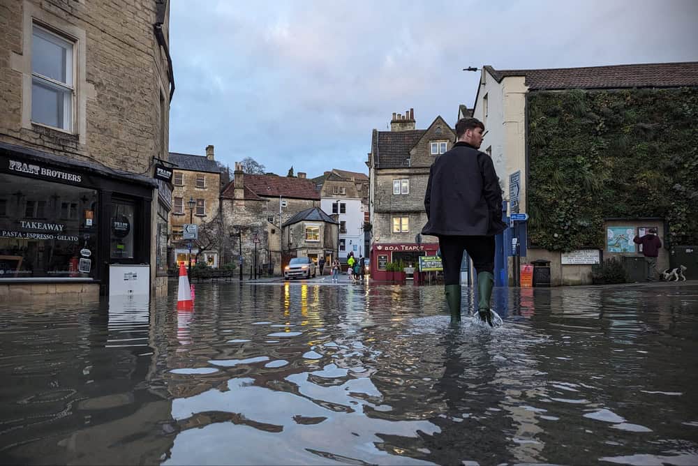 A man wearing wellington boots wades through deep floodwater on a submerged street on January 5, 2024 in Bradford-on-Avon, Wiltshire, United Kingdom. The River Avon burst its banks following heavy rainfall from Storm Henk, flooding local historic town centre businesses including Feast Brothers and the BOA Teapot.