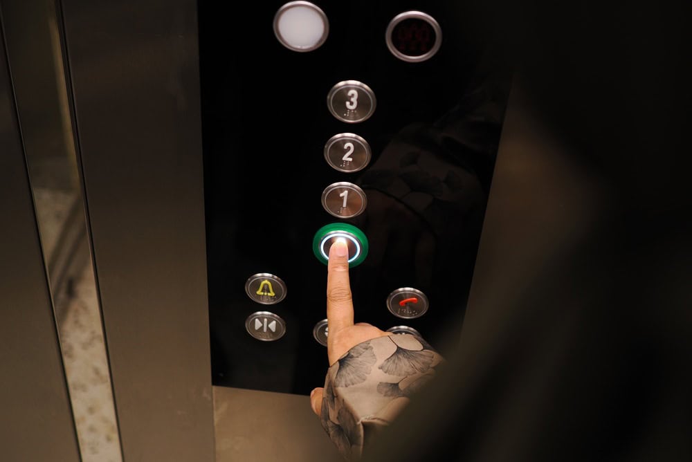A person presses the button for ground floor in a modern elevator at night.