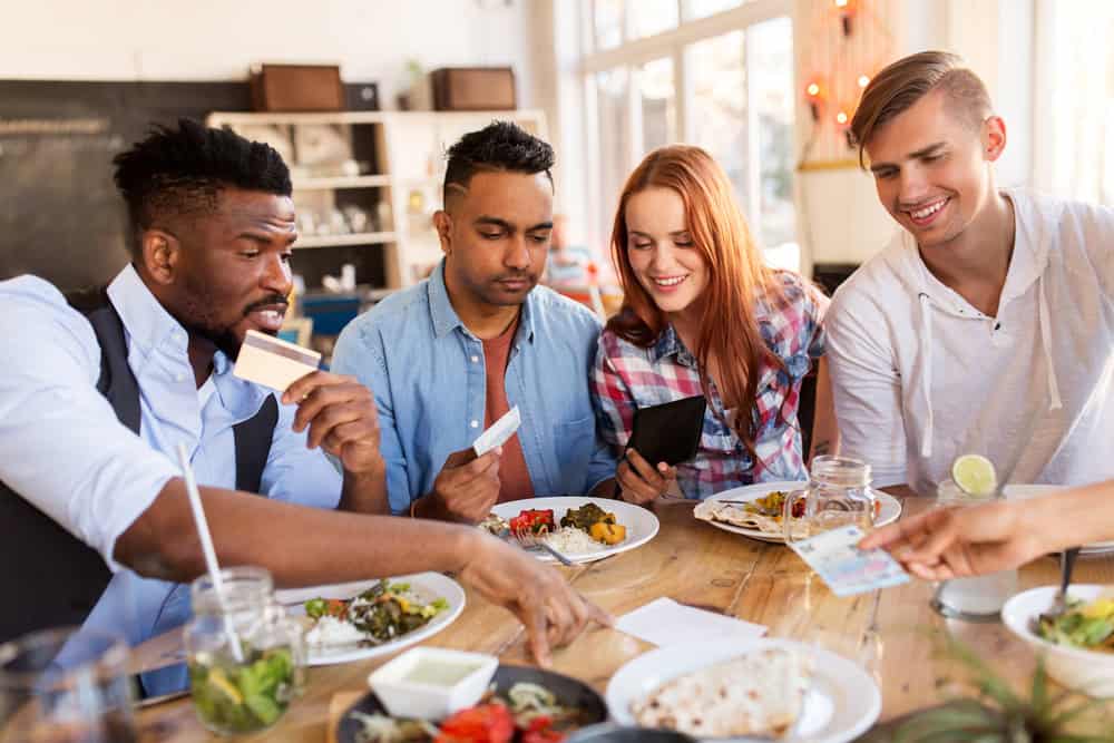 leisure, payment and people concept - happy friends with money and credit card paying bill for food at restaurant