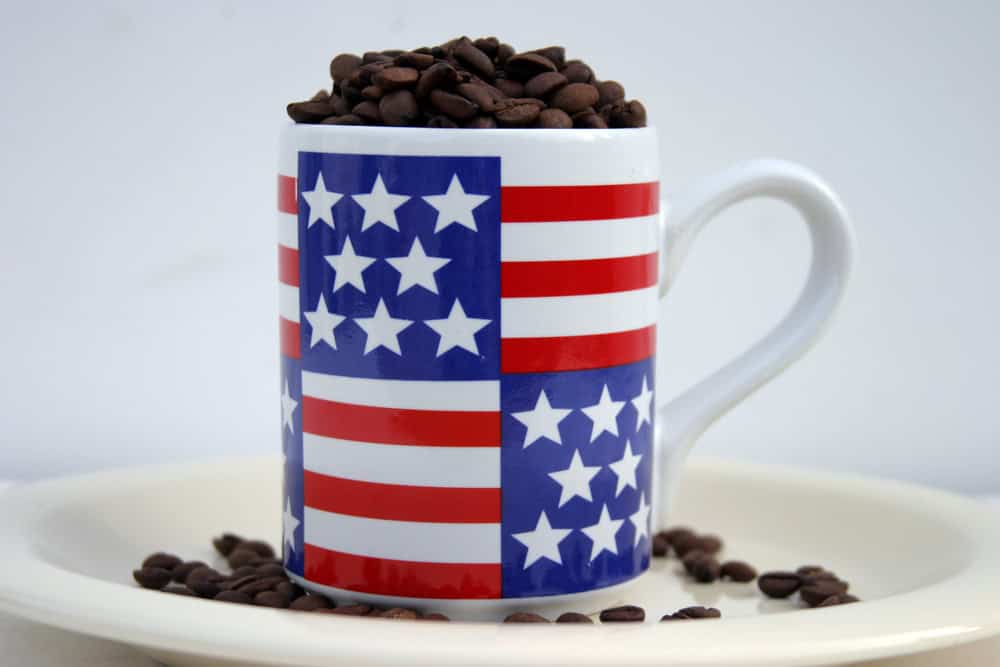 unground coffee beans in and around an American Flag cofee cup on white background